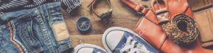 An array of clothing: blue jeans, shirt, compass, watch, handbag, belt, wallet, sneakers