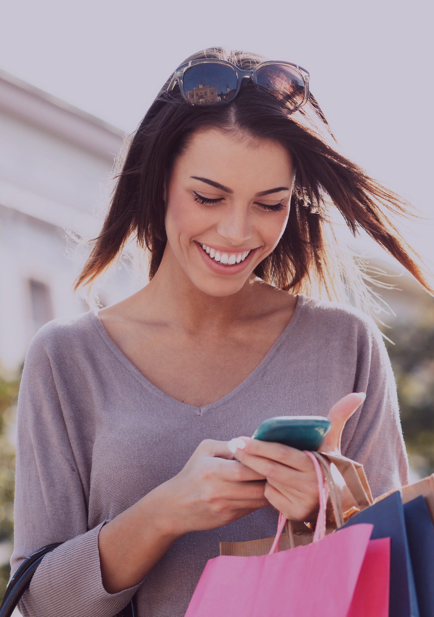 Young smiling woman checking her cell phone, holding shopping bags