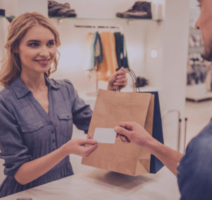 Young woman cashier handing bag and credit card back to customer