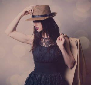 Young woman, wearing brown hat and black lace top dress, holding shopping bags